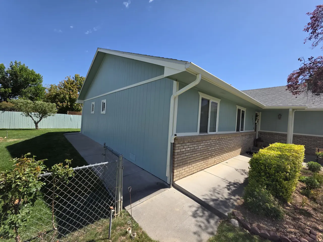 Side of a home with light blue siding over brick and white gutters