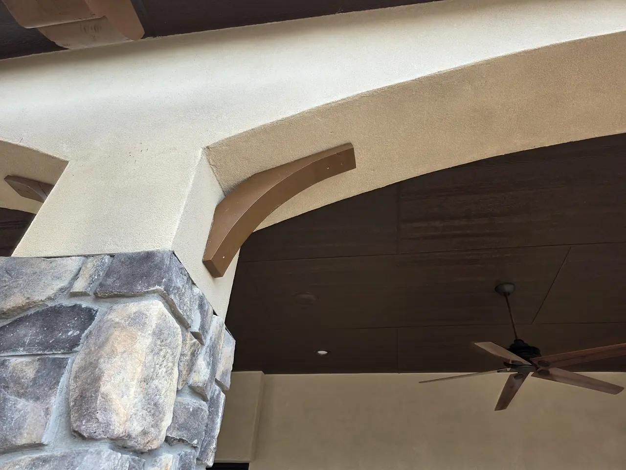 Stained wood corbel and dark soffit against stucco and stone